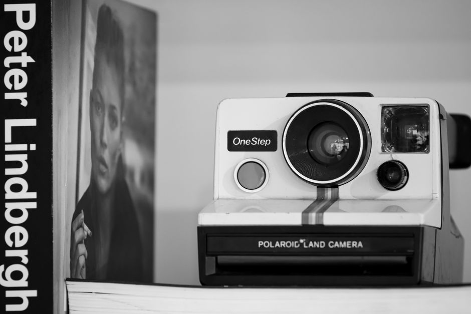 Black and white photo of a Polaroid camera and photography book, artistic composition.