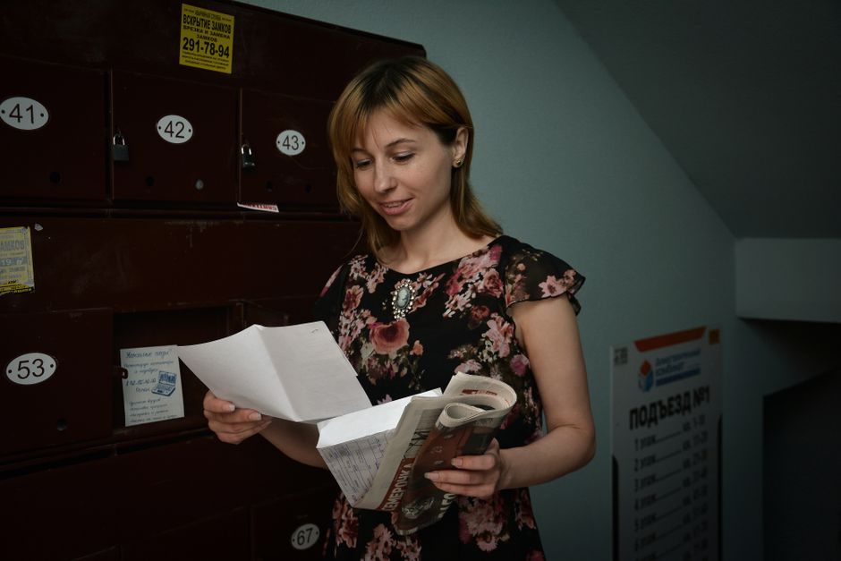 A woman in a floral dress reads mail near vintage lockers indoors, appearing focused and pleased.